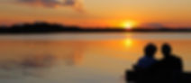 It shows an older couple enjoying a beautiful sunset on a lake.
