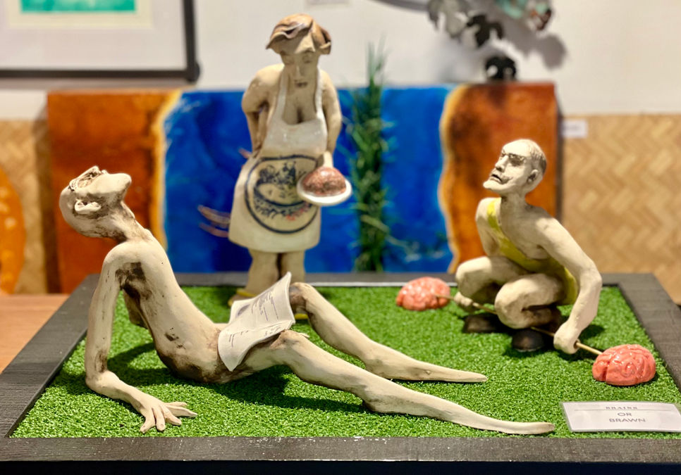 Ceramic figures. Woman serving man brawn pate, he reads recipe, the strong man lifts brains with brawn