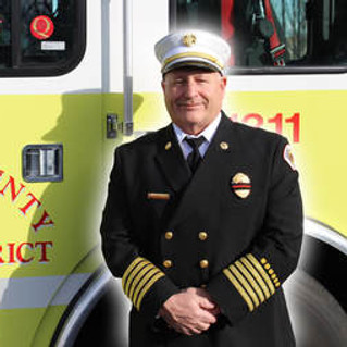 Fire Chief Jim Stucky standing in front of a fire engine in his dress uniform and hat.