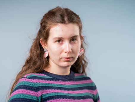 A woman with brown hair and a stripy jumper, stares down the lens with a serious expression.