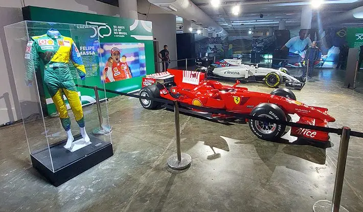 Macacão verde e amarelo em vitrine ao lado de uma Ferrari vermelha