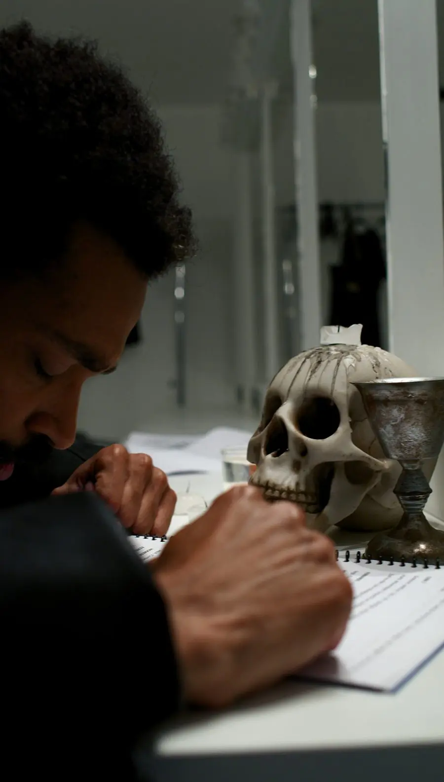 Bastidor de Hamlet: ator debruçado sobre o roteiro ao lado de uma caveira