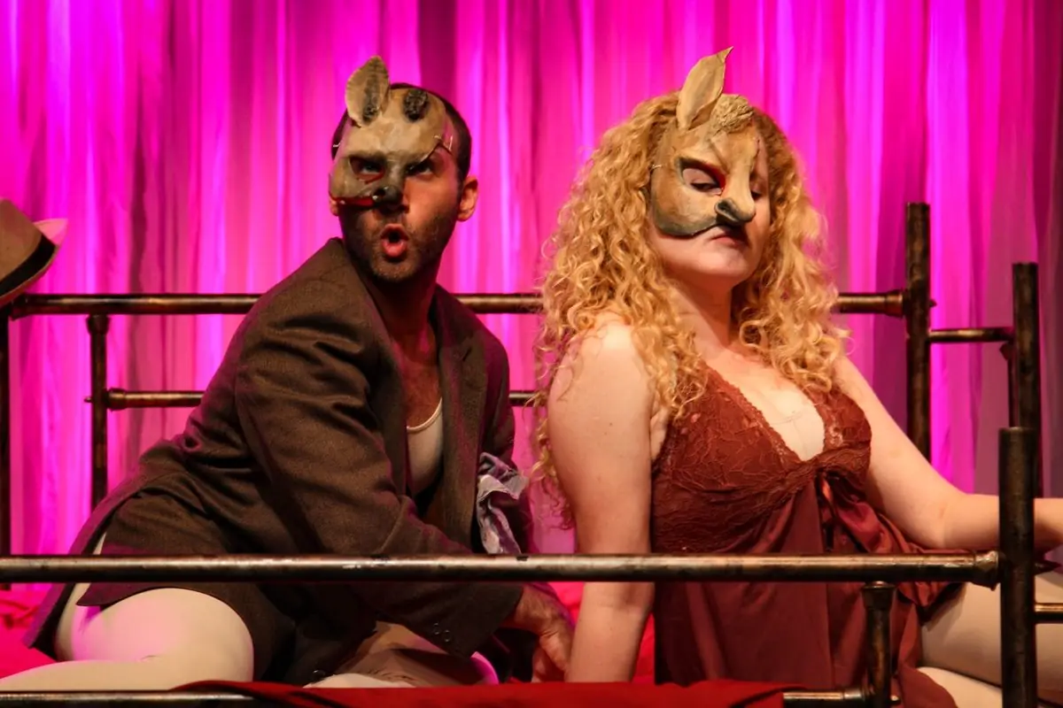 Cena com dois atores mascarados sobre fundo rosa