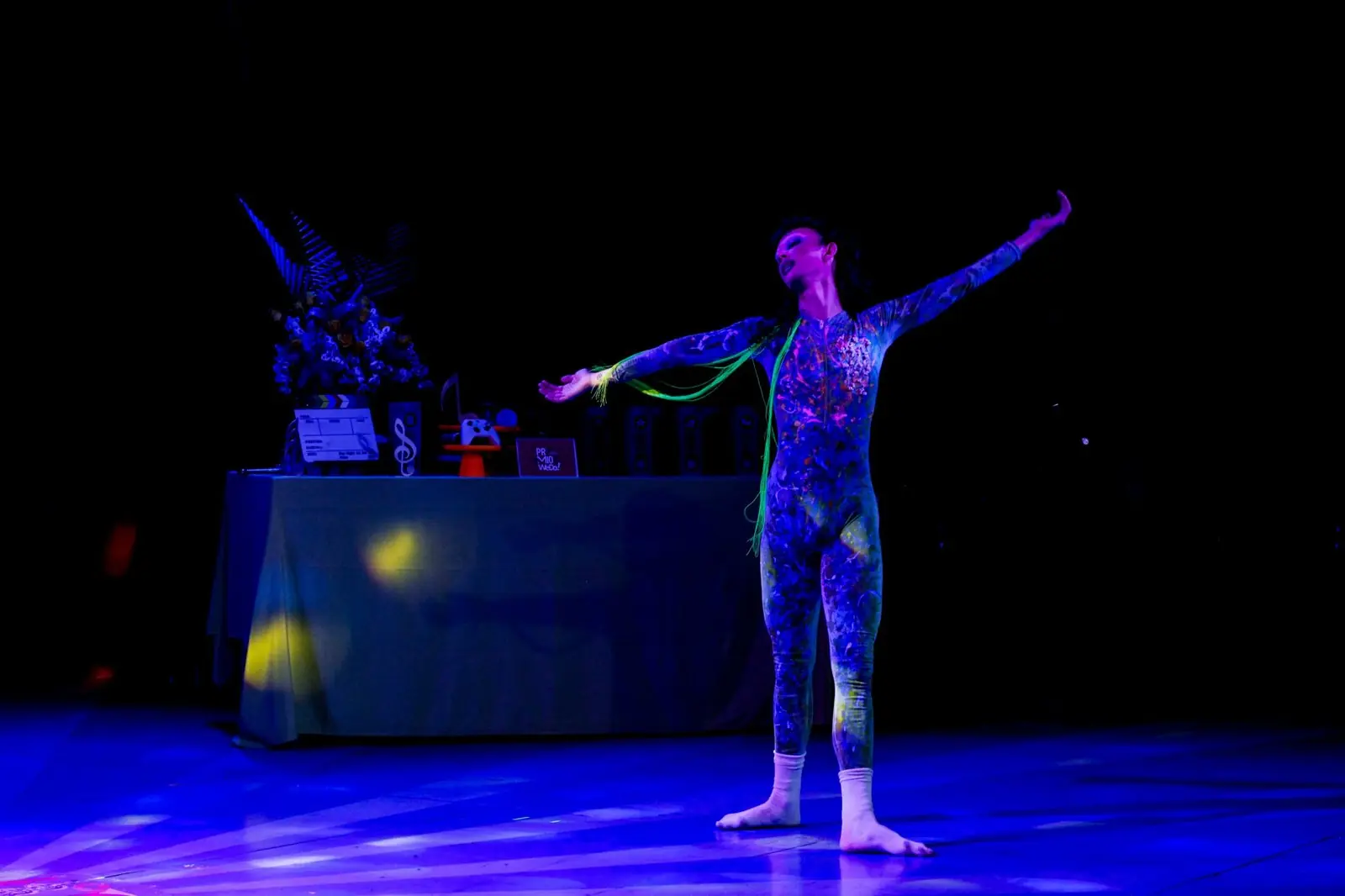 Brun Willi de braços abertos no palco da cerimônia, sob luz azul, com os troféus ao fundo