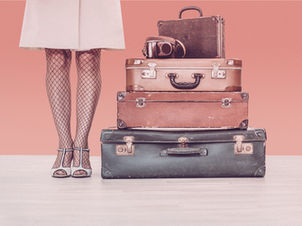 A pile of vintages suitcases next to the lower legs of a woman