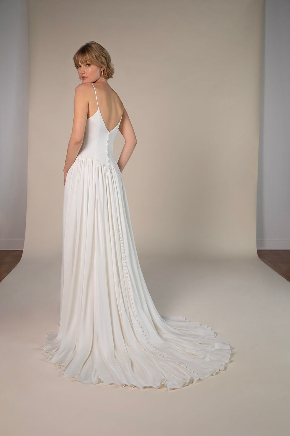 Gisele by All Who Wander – elegant ivory wedding dress with deep V-back, soft draped satin skirt, and chapel-length train.