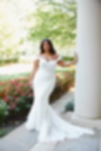 Bride posing in the Essense D3960 lace fit-and-flare wedding dress with off-the-shoulder neckline and long train beside a gar