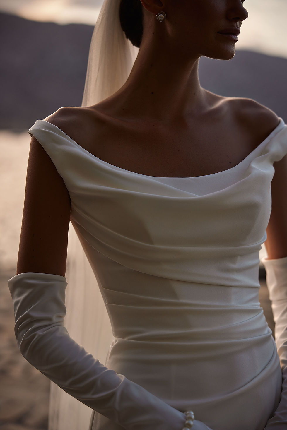Thumbnail: Ilenia by Milla Nova wedding dress highlighting the draped off-the-shoulder neckline and pleatedsatin detailing on the fitted