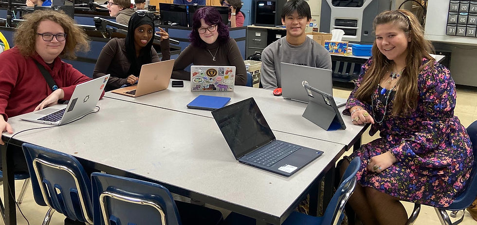 5 members in the CAD room with devices in front of them which they are using to write this newsletter as well as get sponsorships, smiling for the camera.