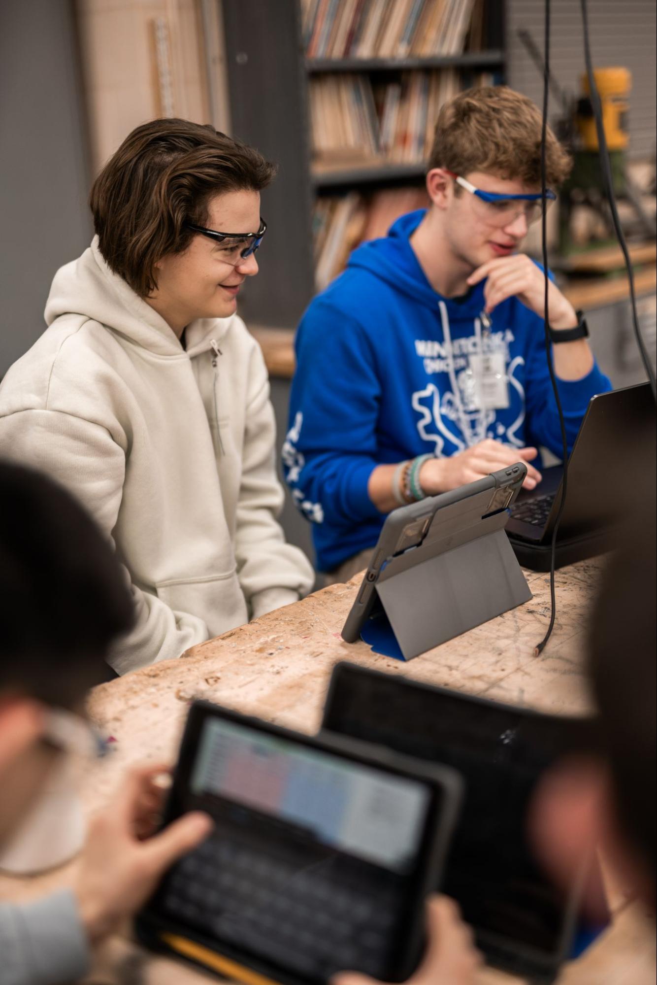 Three boys are pictured wearing safety glasses looking at their iPads