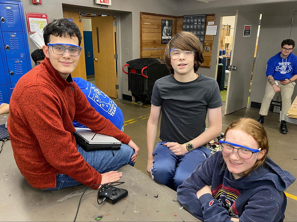 2 members of the programming team with their captain in the metal shop pausing the work and smiling for the camera.