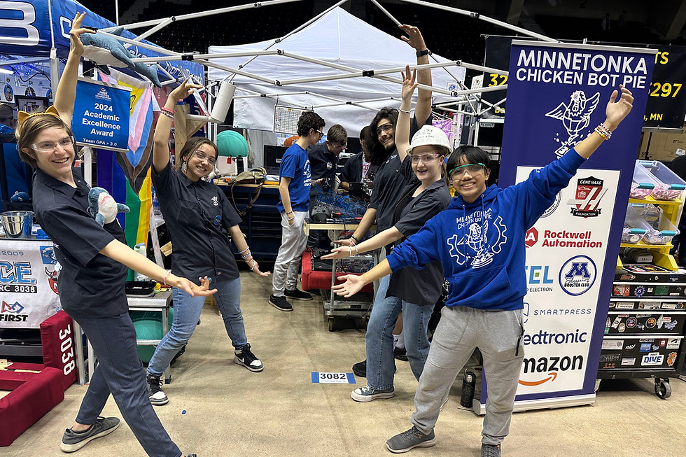 Photo of four team members with their arms wide as to show off the team's pit behind them