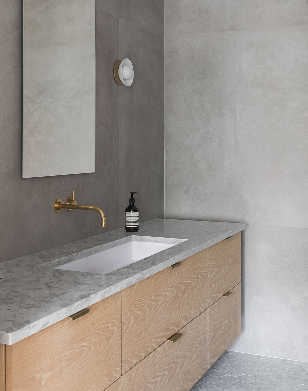 The architects used Nemo’s large-format Area porcelain tiles on the walls. The floating vanity countertop echoes that of the kitchen—honed Carrara marble. The faucet is from California Faucets and the sconce is Allied Maker’s Flush Dome.