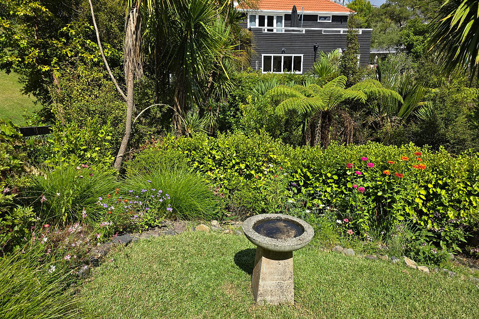 A corner garden bed with flowers and a house in the background