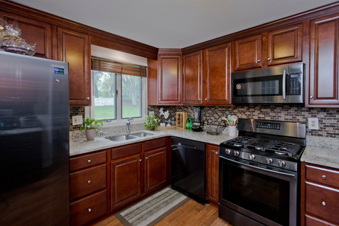 Cherry wood cabinets with stone counters, stainless steel appliances, and tile backsplash.  