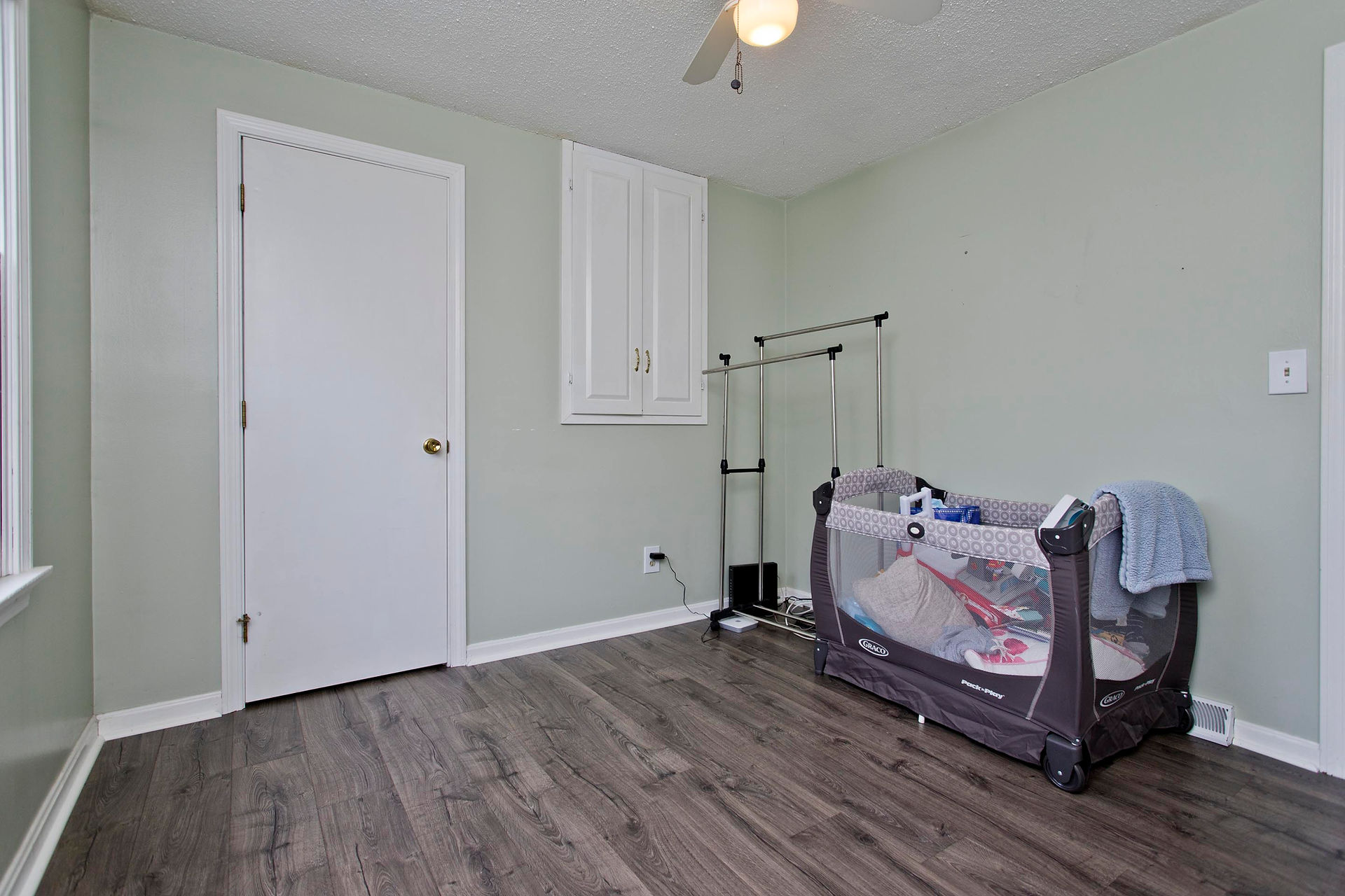 Light grey room with built in wall cupboard and wooden floors. Trim is sharp and white. 