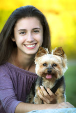 Delaney, a female teen, smiles brightly while holding her tea cup Yorkie dog. A bright yellow background highlights them both. Westford, MA