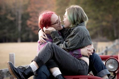 Trans queer partners hug each other while sitting on top of an old tractor during a fall engagement shoot