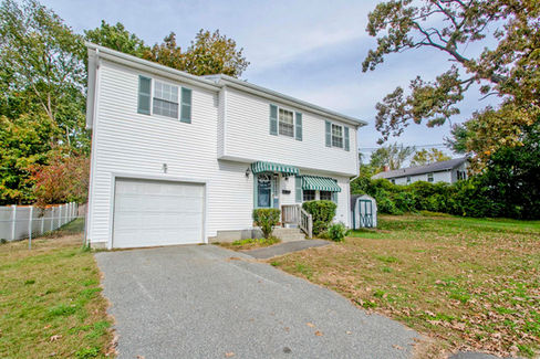 A white sided two story home in Chicopee MA. There is a sidewalk in front of the house and off street parking both as attached garage and driveway. There's a small shed to the side. 