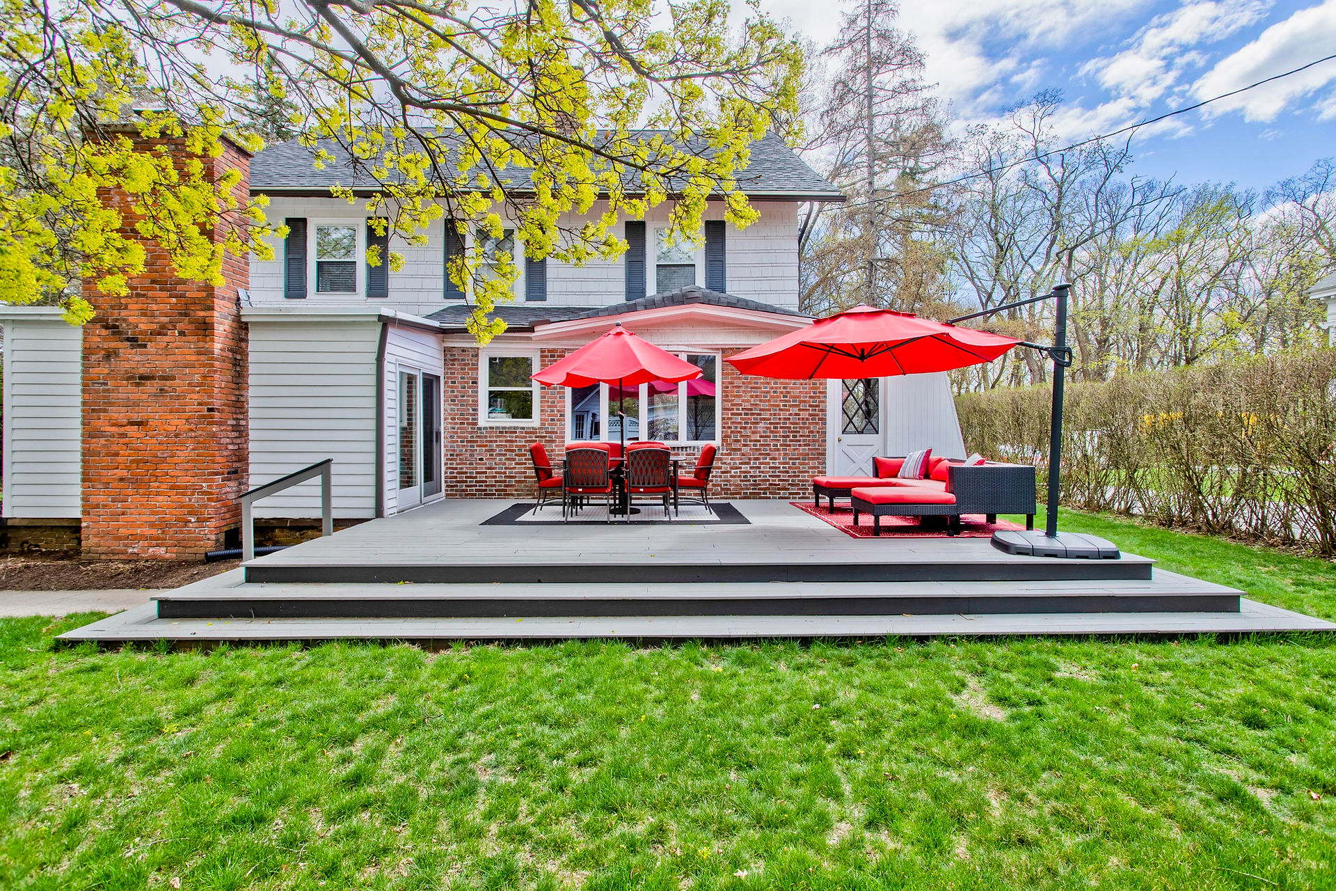 A large, grey open back porch in the Pioneer Valley. There's red lawn furniture and bright blue skies.