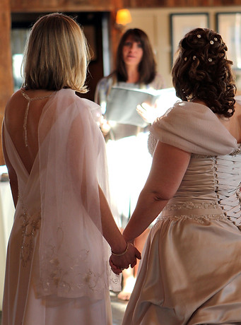 Two LGBT women hold hands as they look forward at their officient on their wedding day