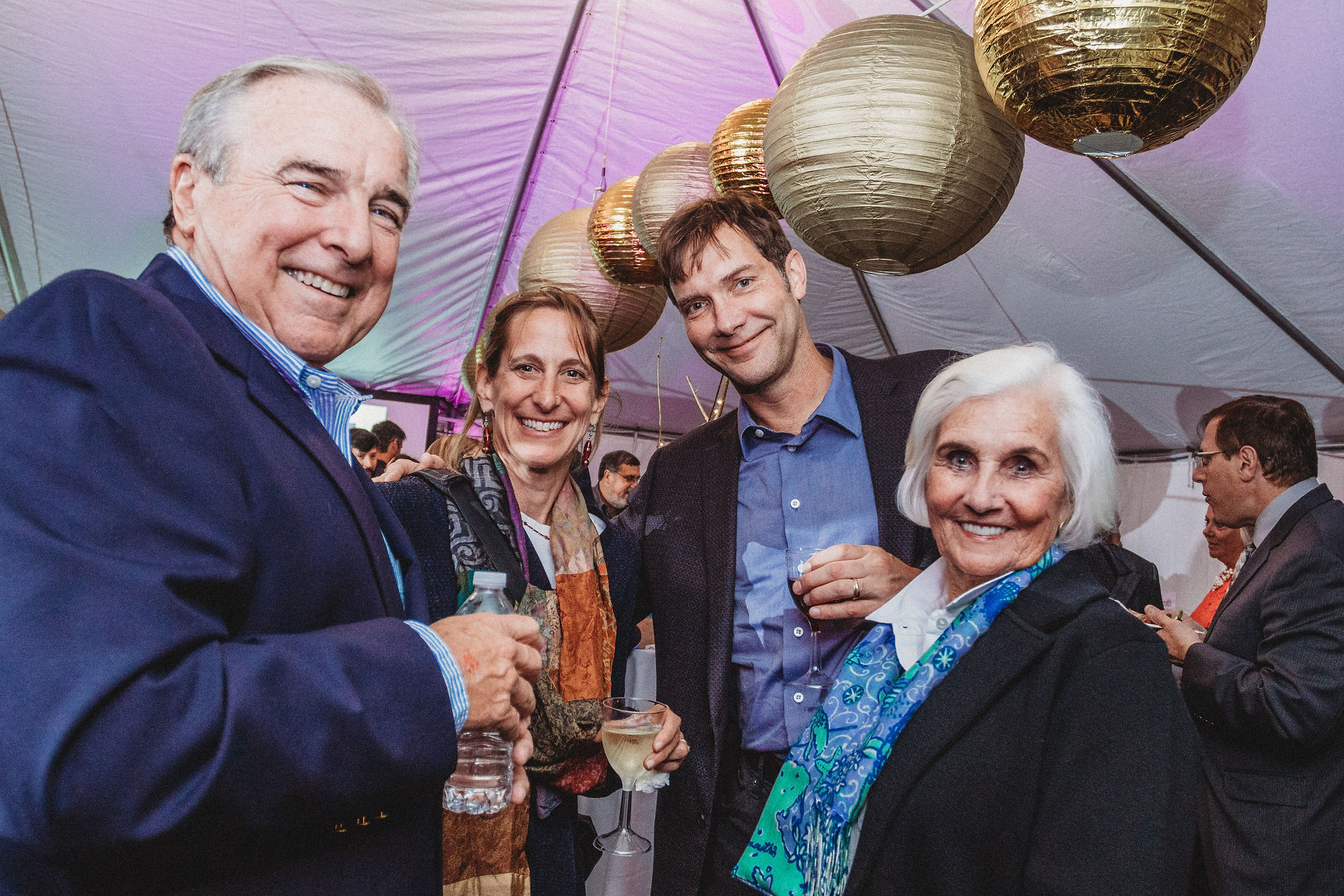 Group of four smile. Behind them are gold lanterns hanging from the tent ceiling.