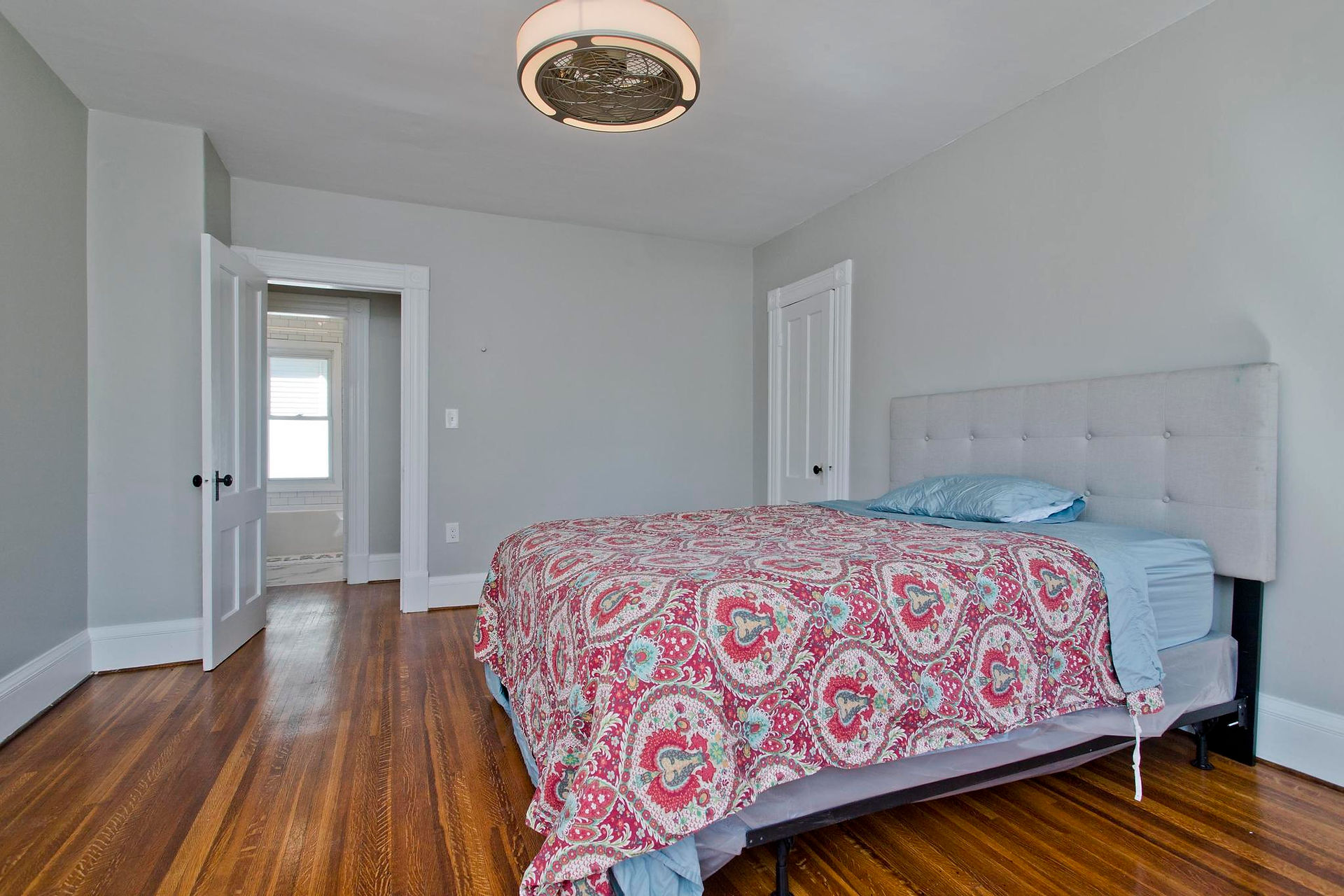 One of the upstairs bedrooms. It has white trim, grey walls, refinished hardwood floors, a ceiling light, and several windows. There's a bed in the center of the room. 