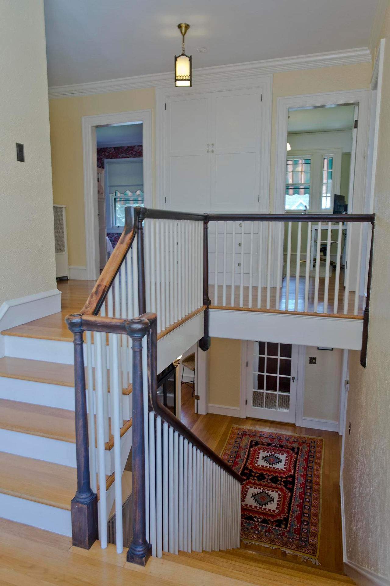 A wide wrapping staircase with white spindles and risers and wood accents. The walls are pail yellow and sconces light the hall. There's polished wood floors.