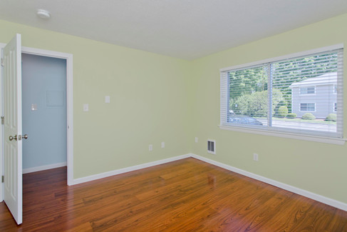 Light yellow bedroom with wood floors and a big window. 