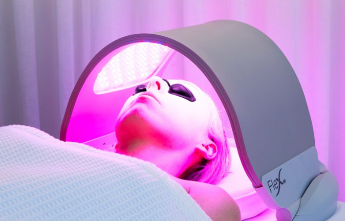 Lady wearing goggles under red light from a Dermalux Flex device