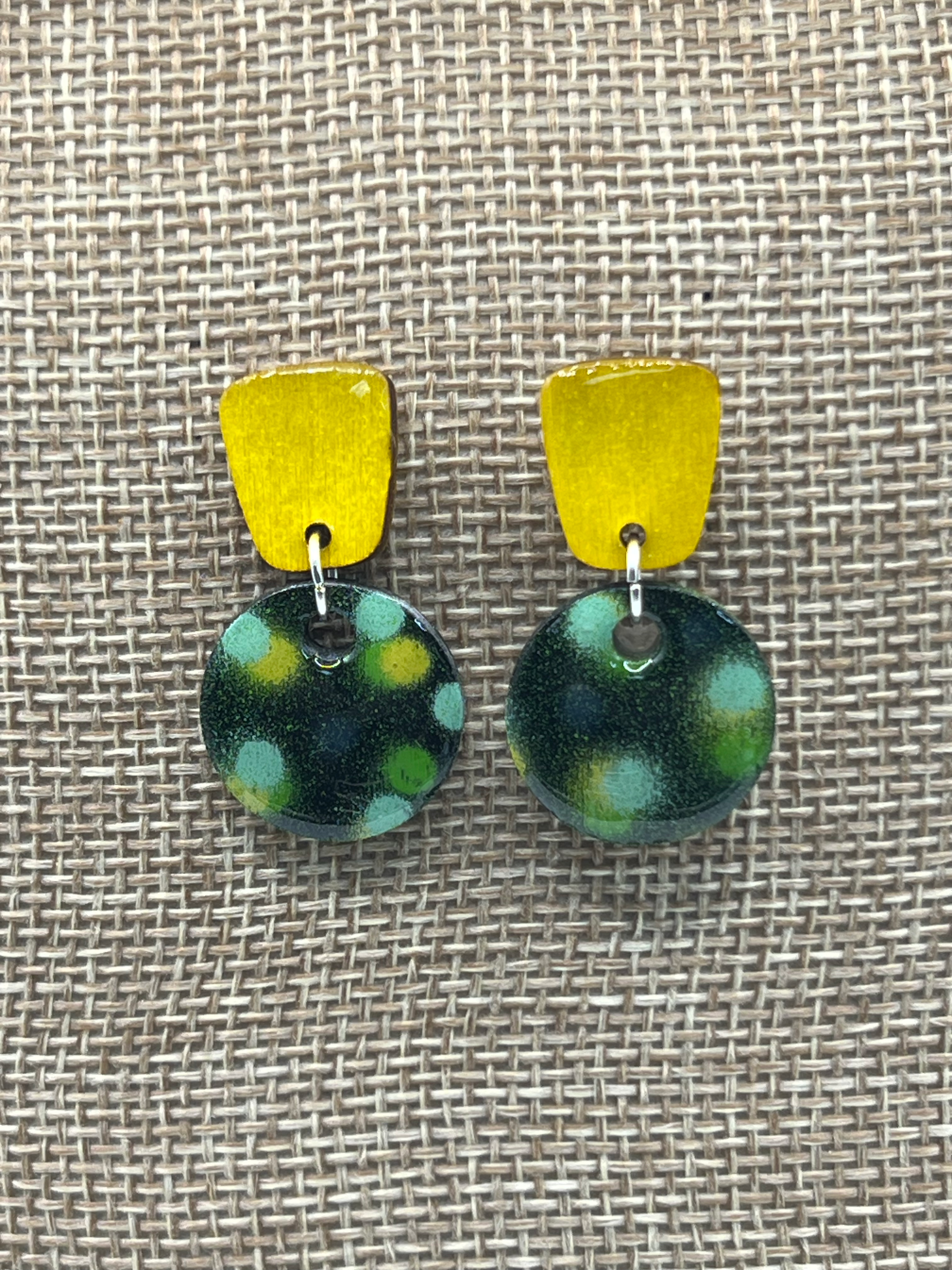 Yellow top and green polka dot earrings on tan fabric background.