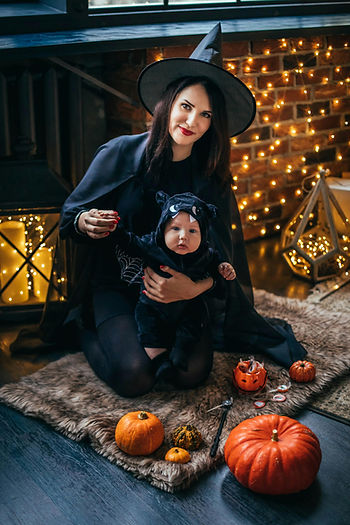 a mother dressed in a halloween witch costume holding a baby dressed in a vampire bat halloween costume onesie