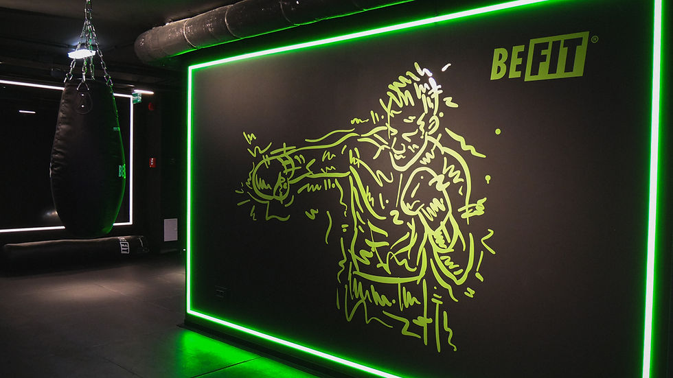Neon green boxer outline on a black wall, labeled "BE FIT." Nearby, a hanging punching bag in a dimly lit gym setting.