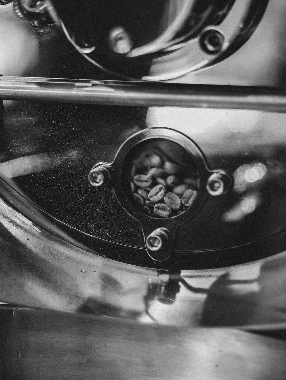Black and white close-up of coffee beans visible through the inspection window of a roasting drum at Ride & Roast