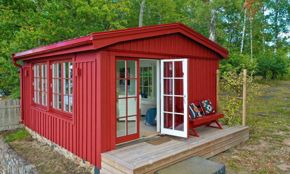 Röd stuga med öppna dubbeldörrar och altan – totalentreprenad fritidshus Småland