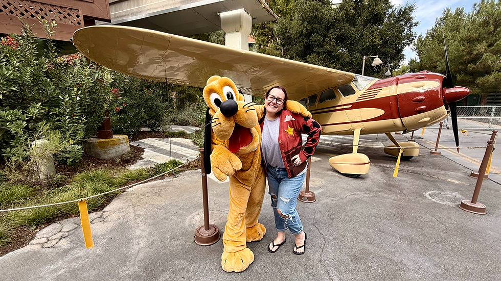 Disney Travel Agent smiling with Pluto costumed character in front of a vintage red and cream plane. at Disneyland California Adventure.