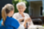 Resident of Silver Spring Personal Care Home sitting in a wheelchair and smiling at the Activities Director while holding hands