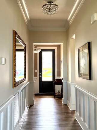 A long hallway featuring wainscaoting, large pieces of artwork, and a small crystal lighting fixture