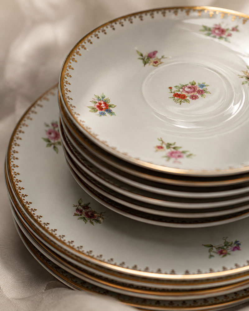 Pratos antigos de porcelana floral empilhados sobre tecido claro em composição de quiet luxury e decoração atemporal.