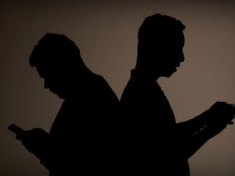 Silhueta de dois jovens mexendo no celular