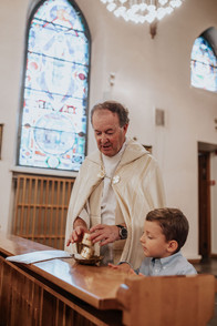 Pappi näyttää isoveljelle perinteitä katolisissa ristiäisissä ristiäisten valokuvauksessa Helsingissä