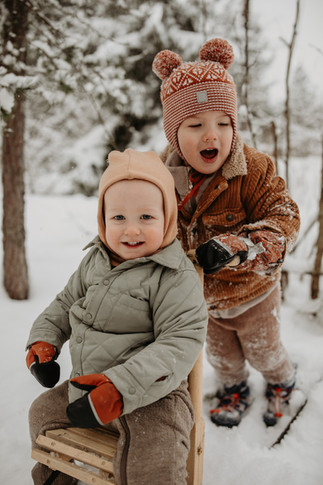 Isoveli työntää pikkuveljeä potkukelkassa lapsikuvauksissa Vantaalla. Kaunis luminen maisema taustalla.