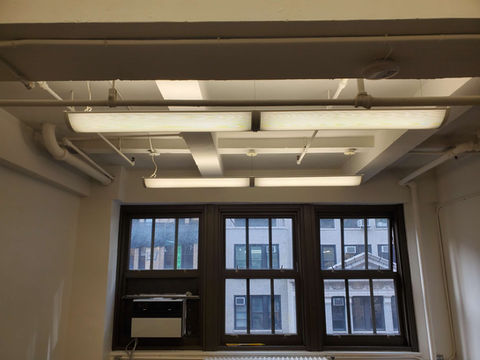 Bright fluorescent ceiling lights illuminate an office space, overlooking a city view.