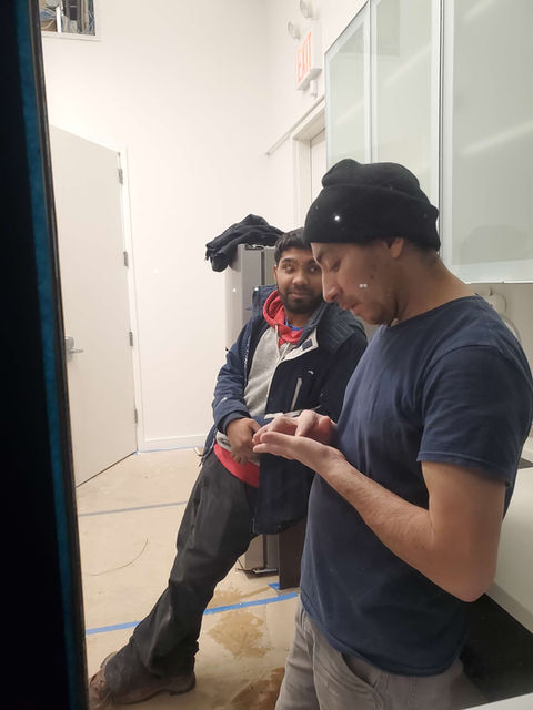 Two men in a kitchen, one looking at his phone