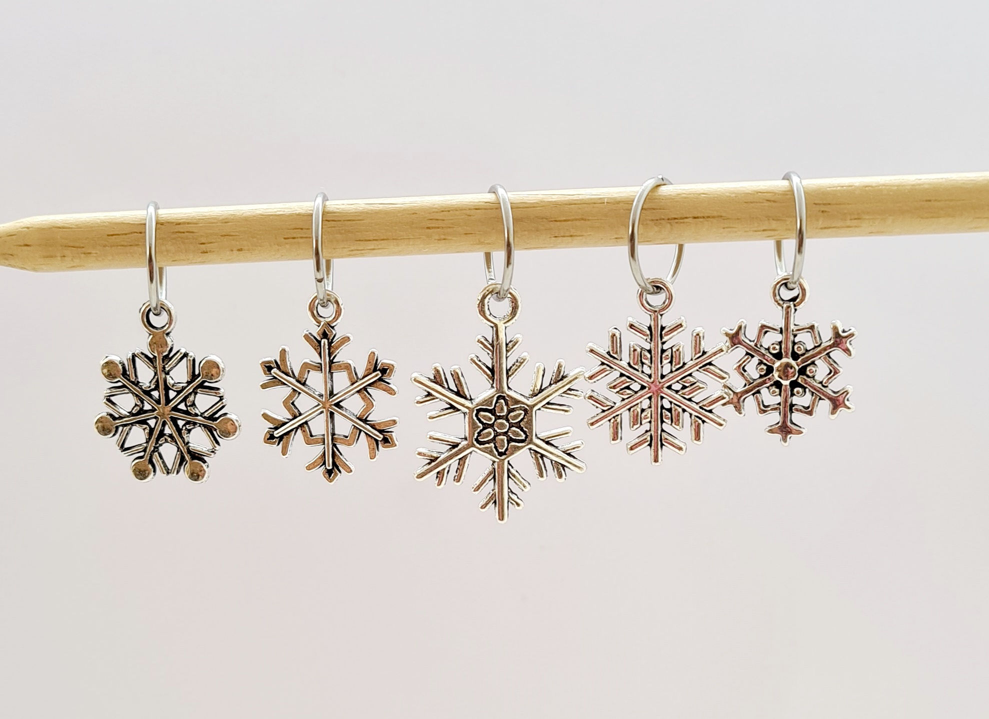 5 assorted snowflake design charms with rings in silver colour on a wood knitting needle