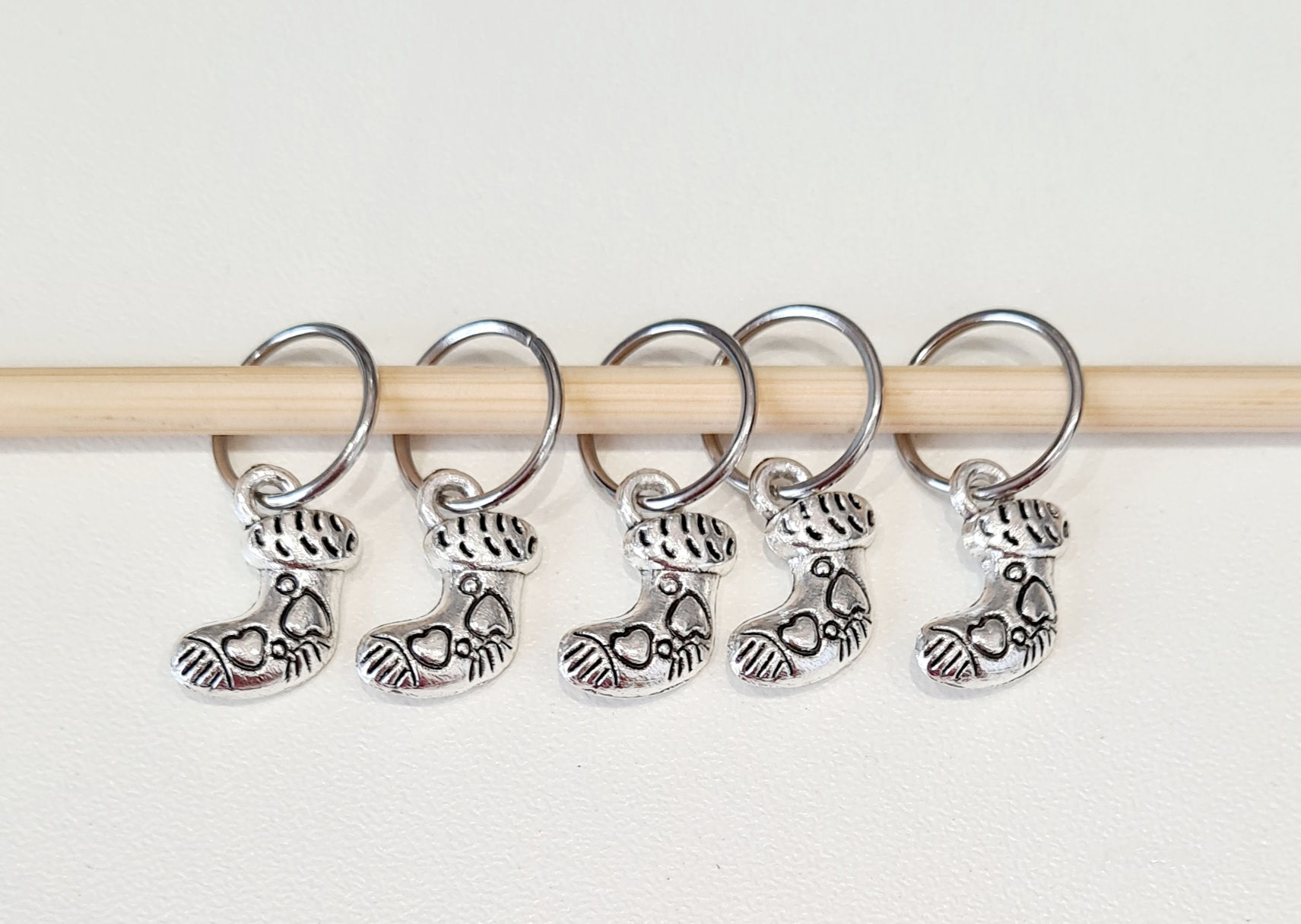 5 sock shaped silver coloured metal charms with rings on a knitting needle