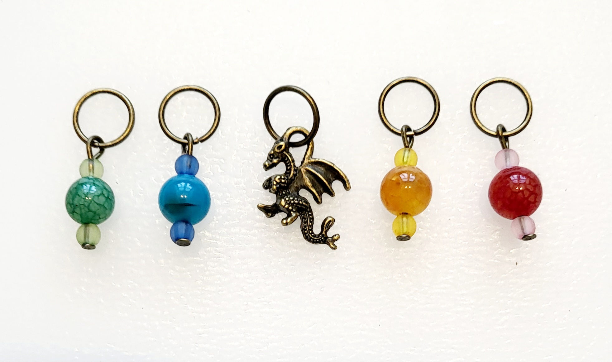 bronze coloured metal charm of dragon with 4 coloured bead stitch markers, 1 each of red, blue, yellow and green on rings