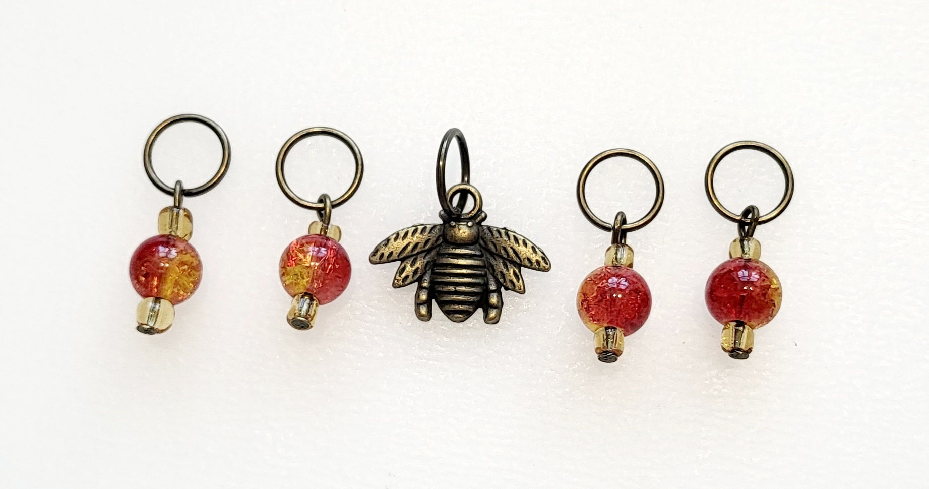 bronze coloured metal bee shaped charm with 4 yellow/orange coloured bead charms all with rings