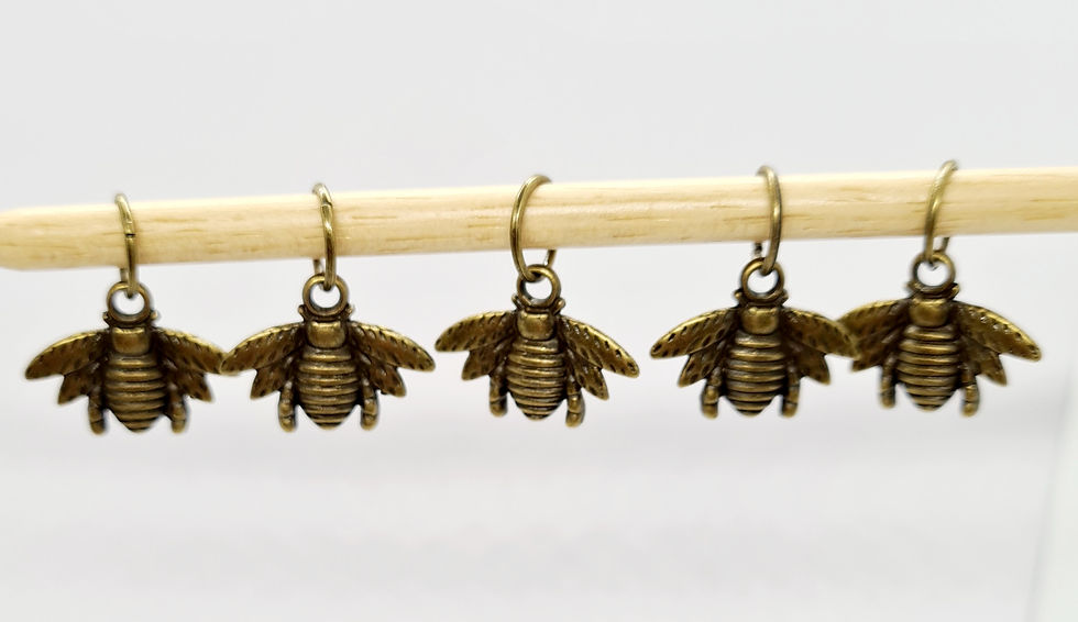 5 bronze coloured metal bee shaped charms with rings on a knitting needle