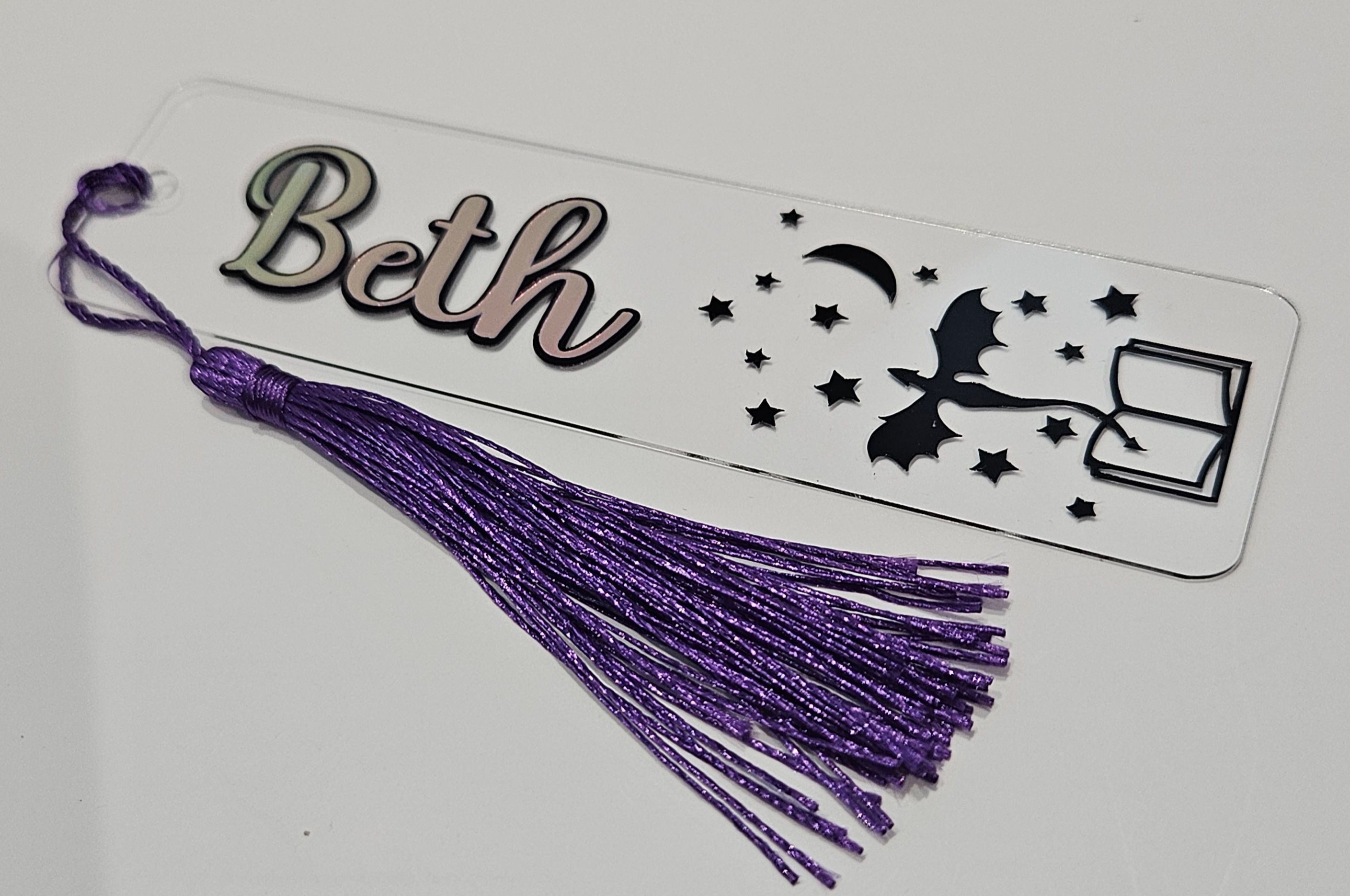 dragon coming out of book with stars and moon decal with name Beth on a clear bookmark with purple tassel